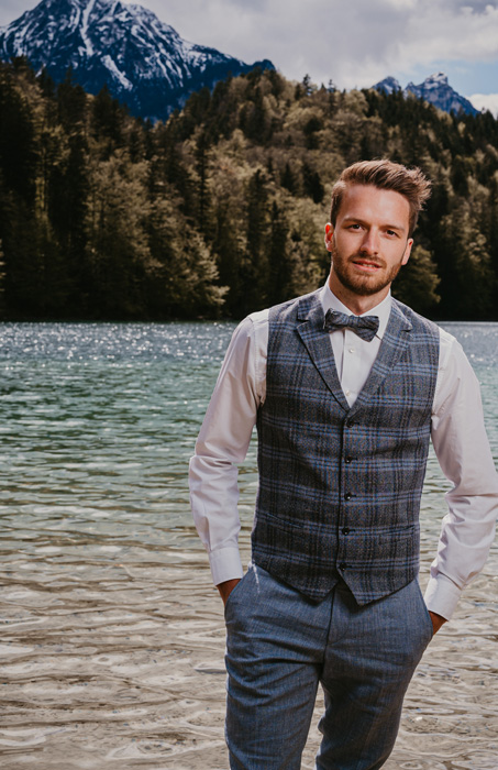 Bräutigam mit Karoweste im Hochzeitsoutfit am Ufer eines Bergsees